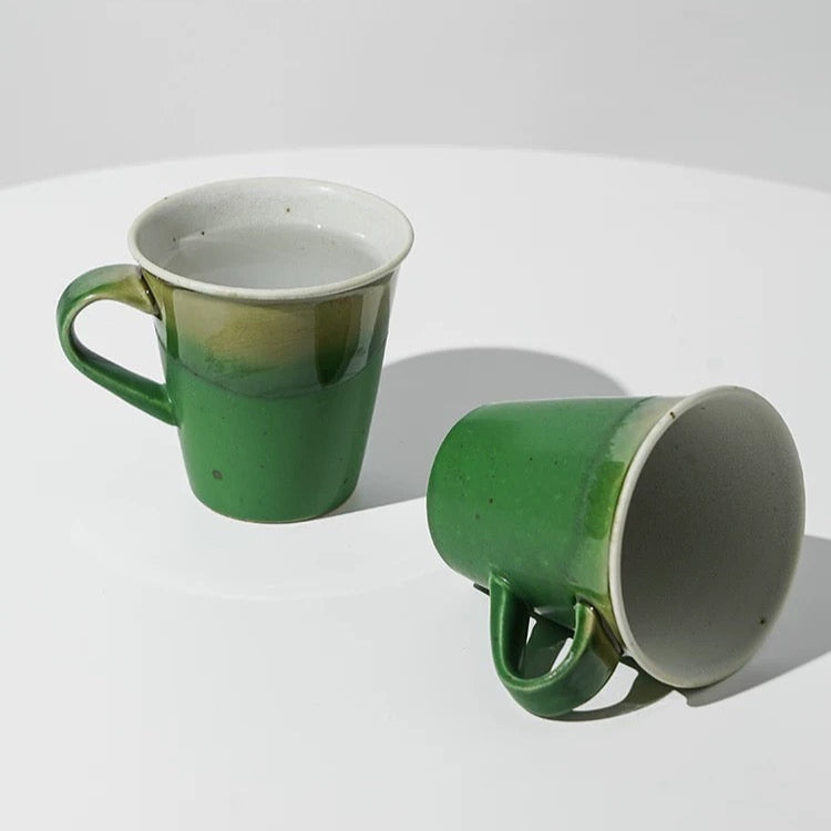 Two green ceramic mugs on a white surface with a light gray background.