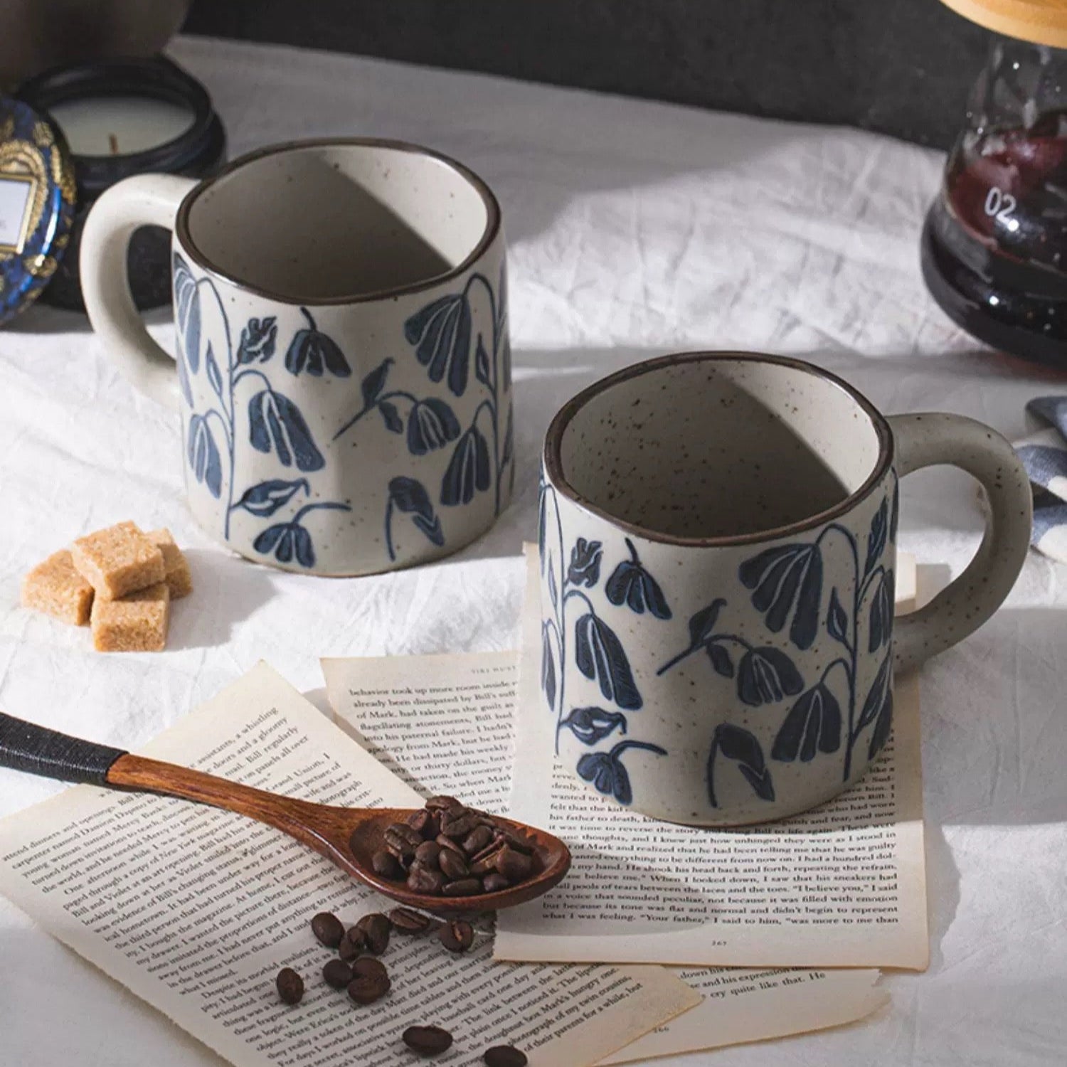 Two ceramic mugs with blue floral patterns on a table with coffee beans and a wooden spoon.