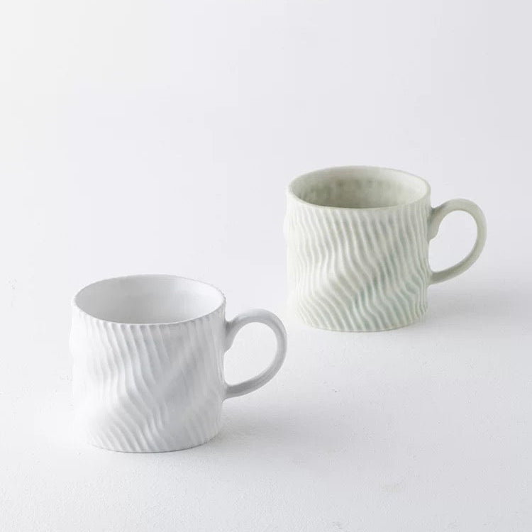 Two white ceramic mugs with textured design on a light gray background