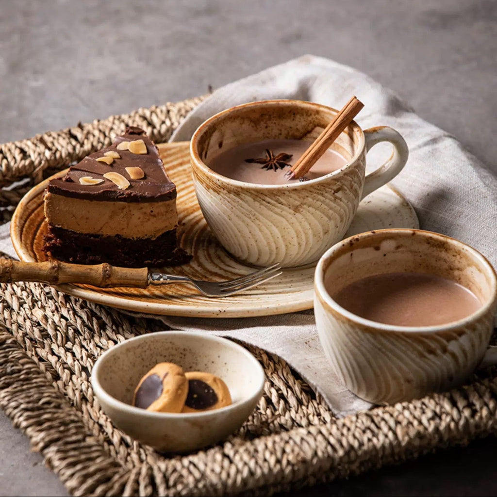 Ceramic tea set with a cup, saucer, and small bowl on a textured surface.