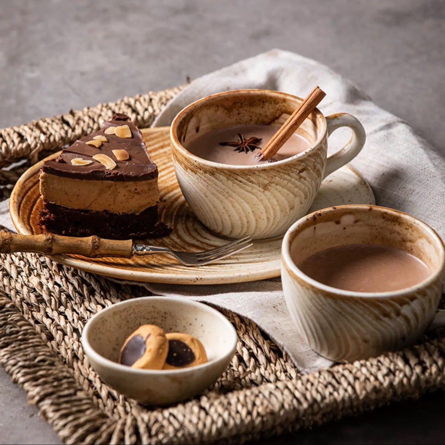 Ceramic tea set with a cup, saucer, and small bowl on a textured surface.