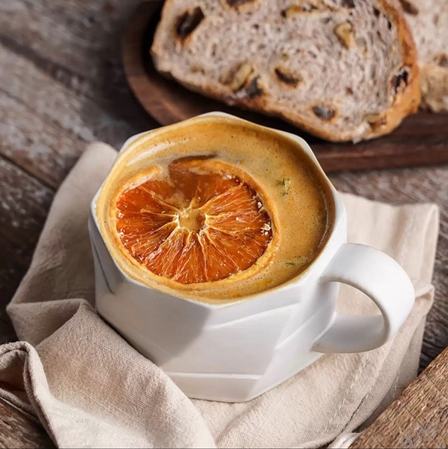 Vintage coffee cup with dried orange slice on a wooden surface with bread in the background