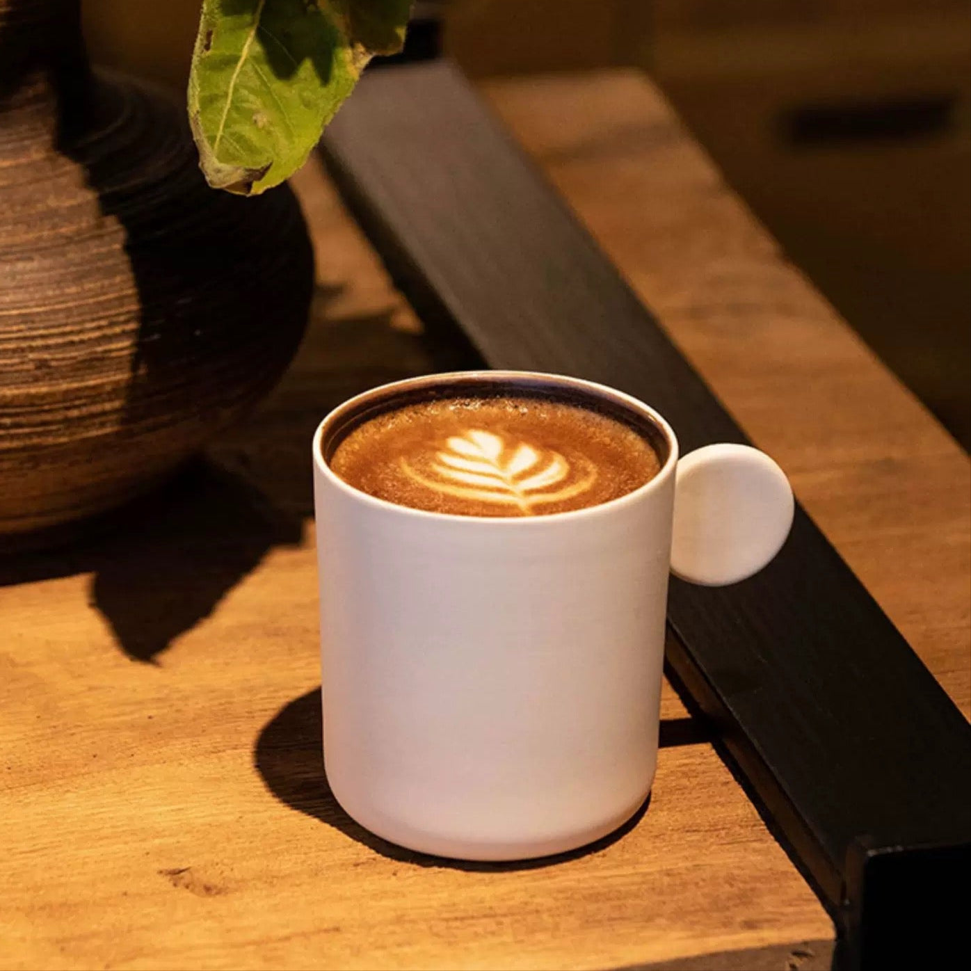 White mug with coffee on a wooden table with a vase and flowers in the background