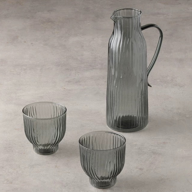 Set of three ribbed glass pieces including a pitcher and two tumblers on a gray surface.