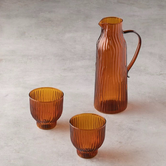 Set of three amber glass pieces including a carafe and two tumblers on a light gray background