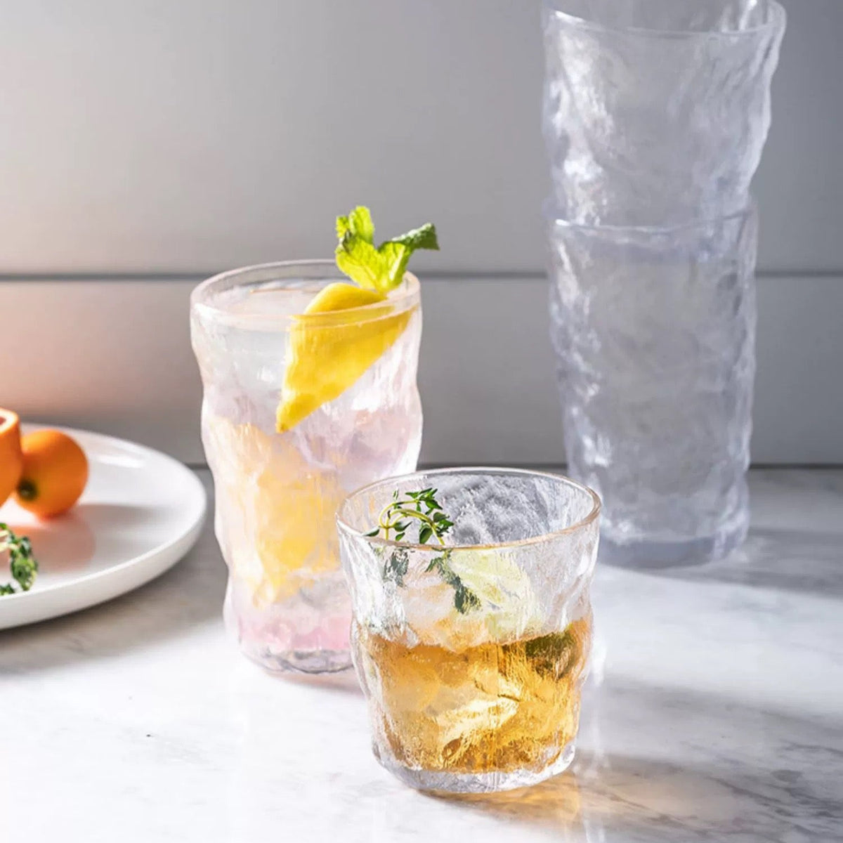 Three glasses with drinks on a marble surface, one with a lemon garnish.